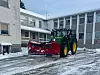 John Deere-traktor med raud snøplog ryddar snø framfor ein bygard