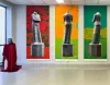 Gallerirom med tre fargerike fotomontasjar av ein statue og eit bystehovud dekt av raudt stoff ved vindauget.